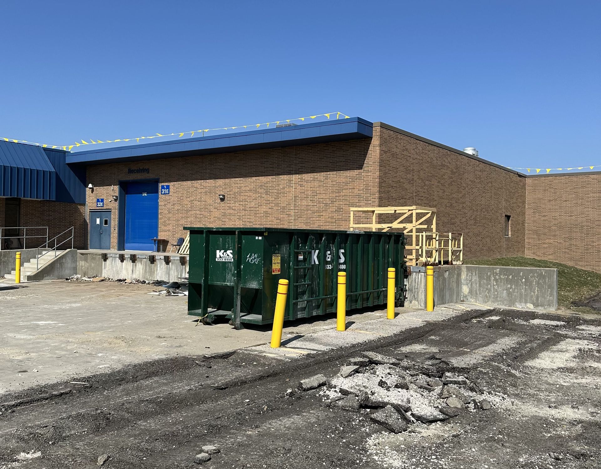 A large green dumpster is parked in front of a brick building.