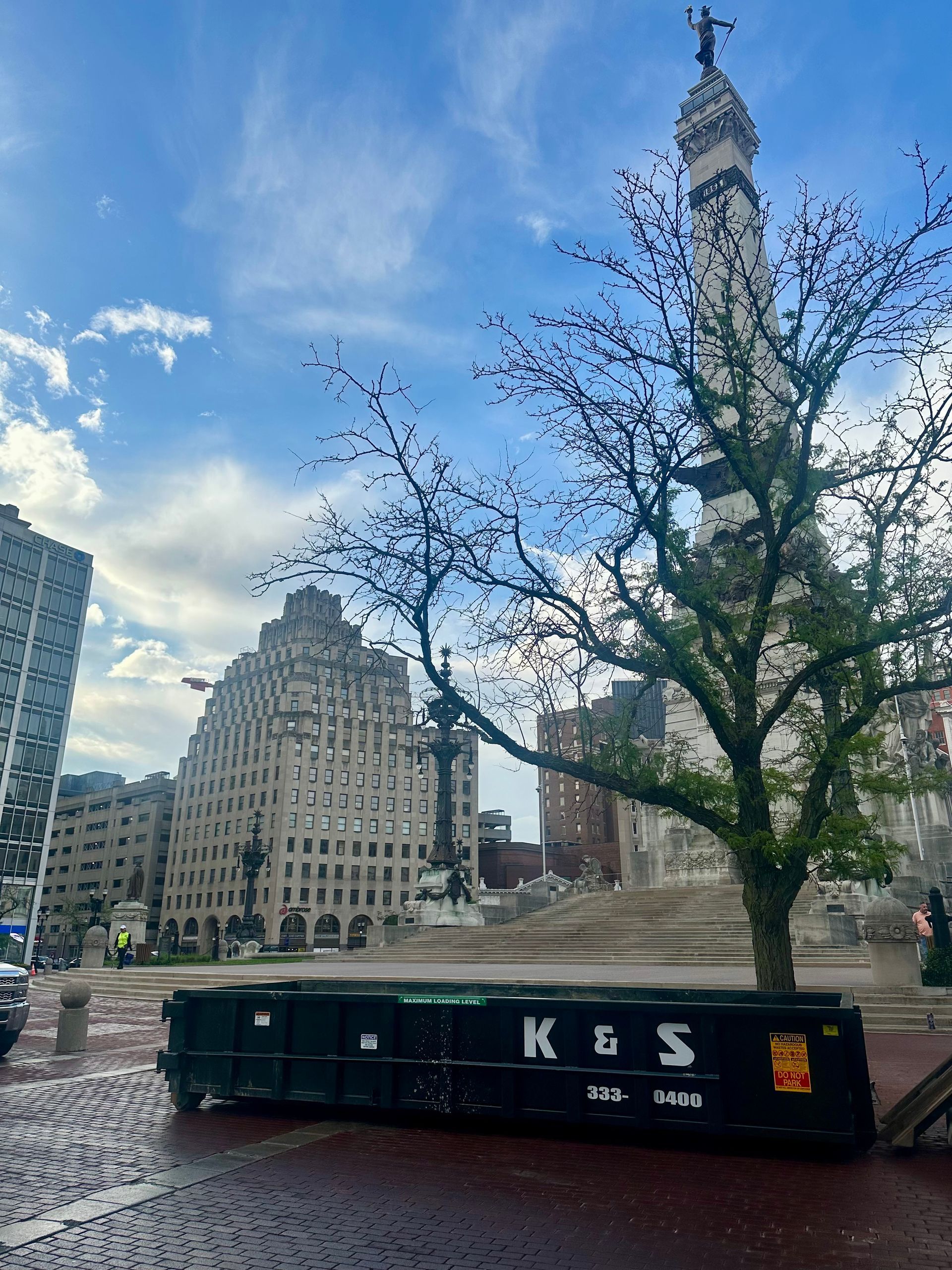 A dumpster is sitting in front of a statue in a city.
