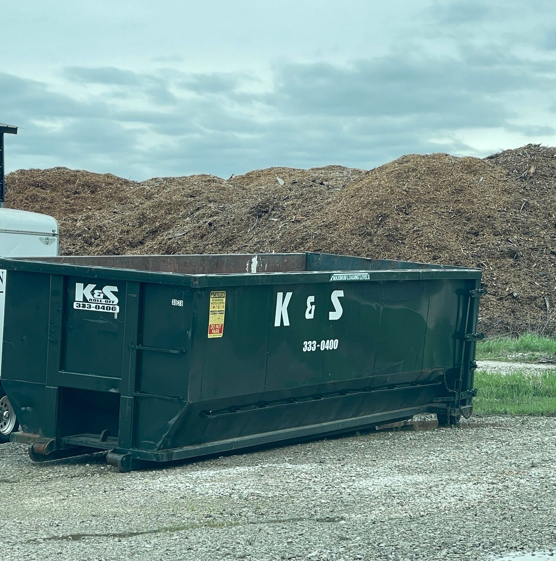 A dumpster that says kes is parked in front of a pile of wood chips