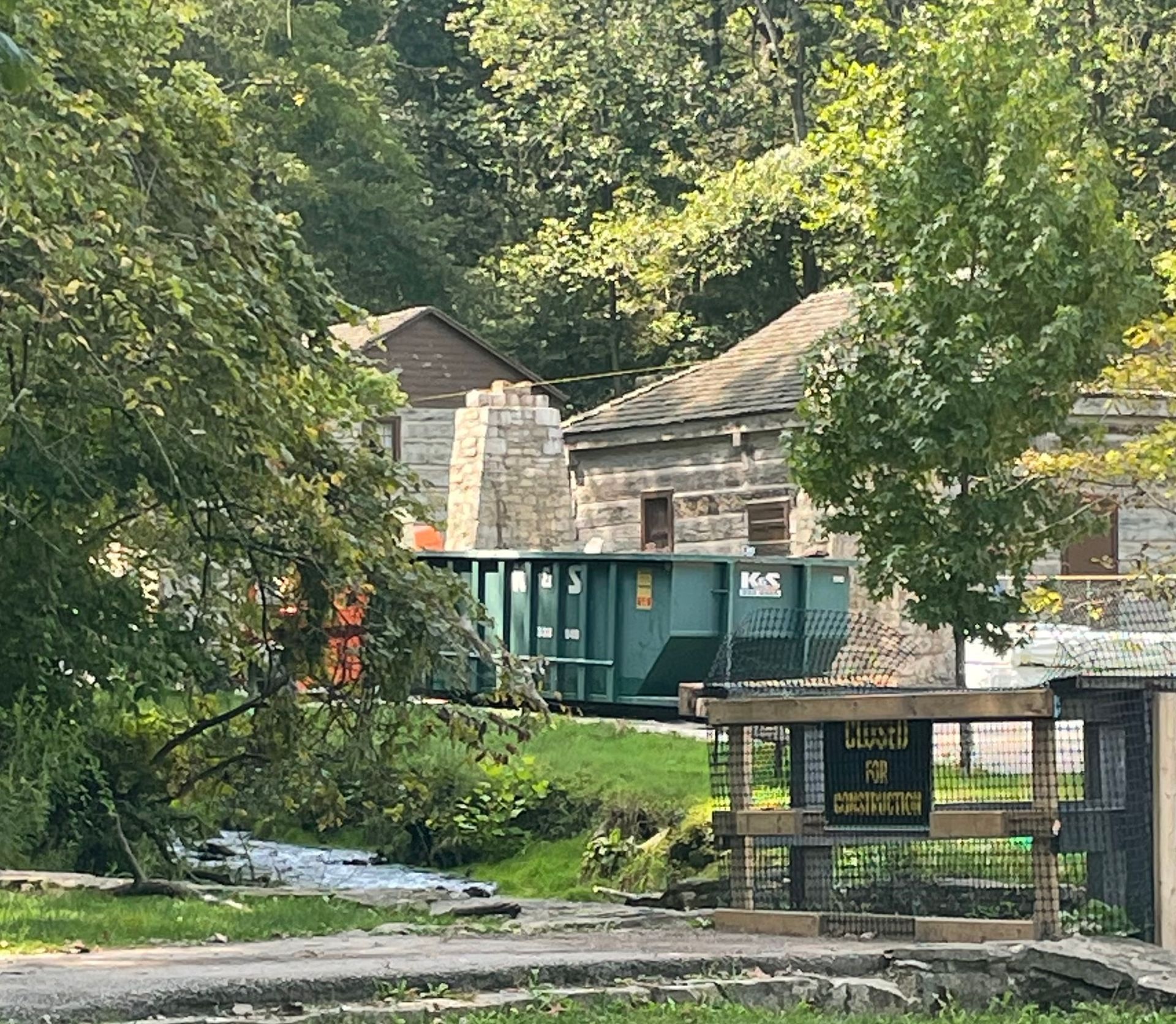 A green dumpster is parked in front of a stone building.