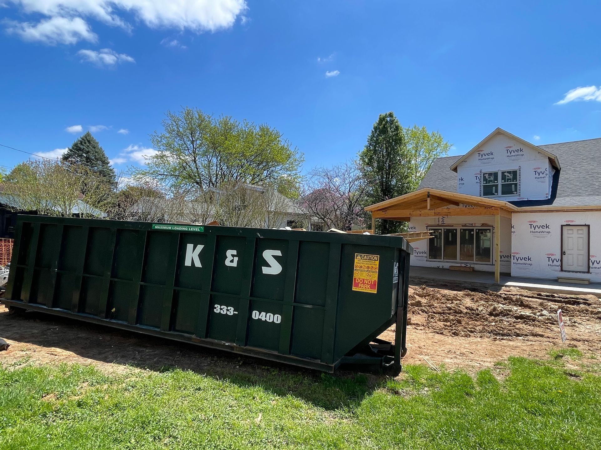 A dumpster is parked in front of a house under construction.