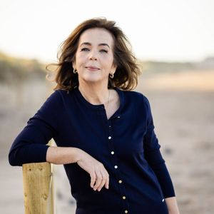 A woman in a blue cardigan leans on a wooden post