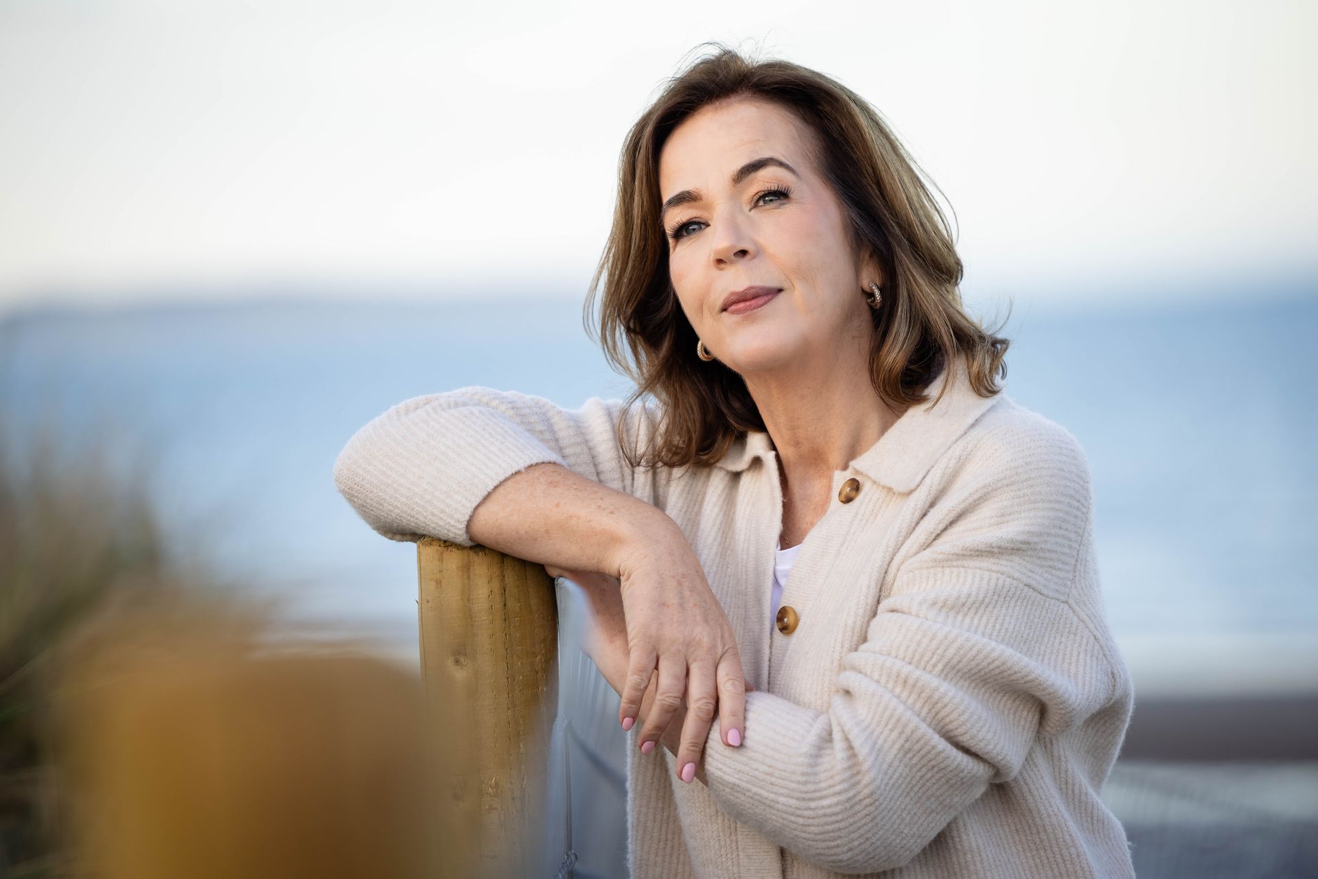 A woman leaning on a wooden railing looking at the ocean.
