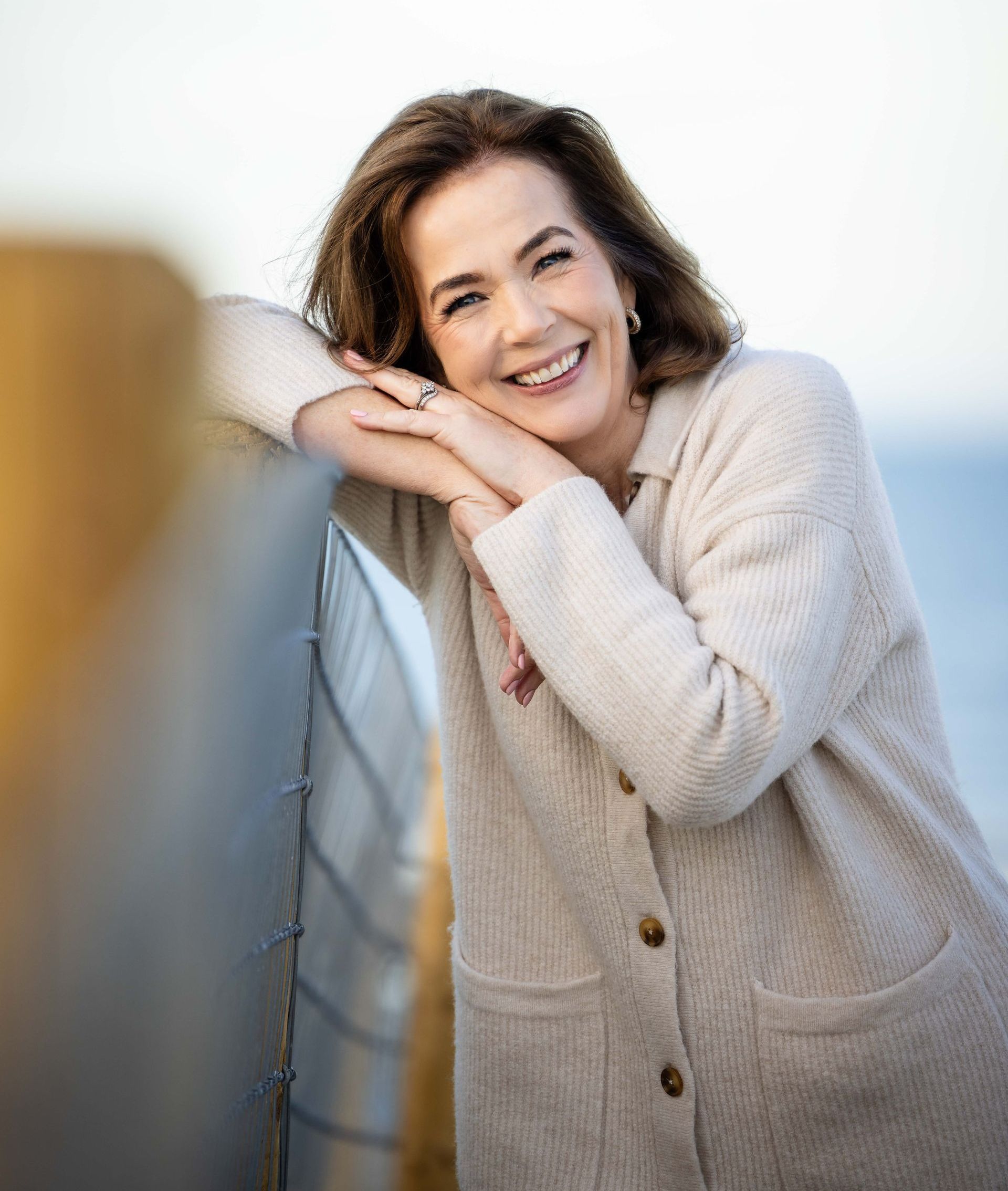 A woman in a sweater is leaning on a railing and smiling.