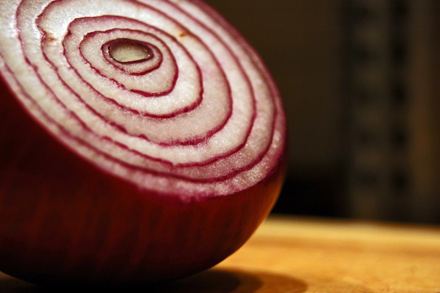 A red onion is cut in half on a wooden cutting board.