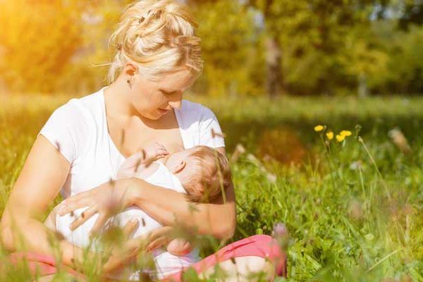 A woman is breastfeeding her baby while sitting in the grass.