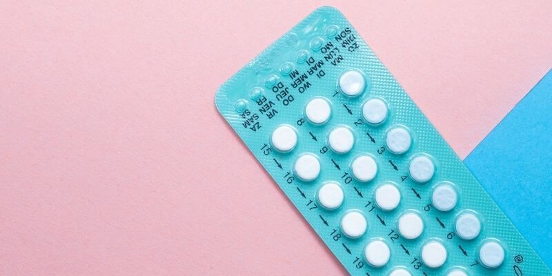 A blister pack of birth control pills on a pink and blue background.