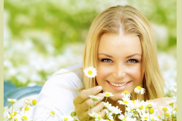 A woman is laying in a field of daisies and smiling.