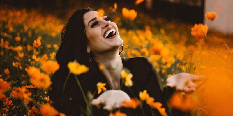 A woman is laughing in a field of flowers.