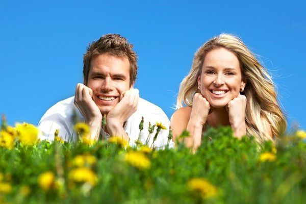 A man and a woman are laying in the grass and smiling.