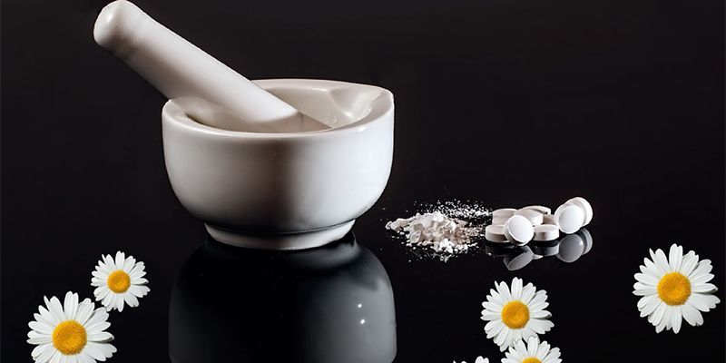 A mortar and pestle surrounded by daisies and pills