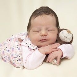 A newborn baby is sleeping with a stuffed animal.