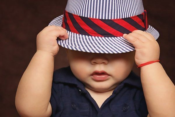 A baby wearing a striped hat covering his eyes