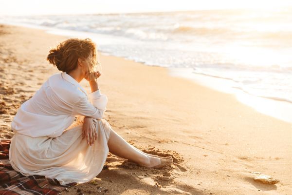 A woman is sitting on the beach looking at the ocean.
