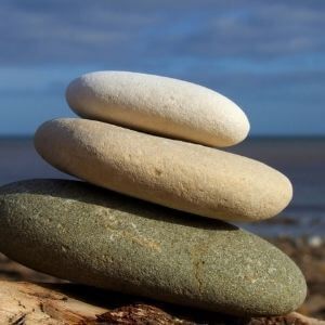 Three rocks are stacked on top of each other on a beach.