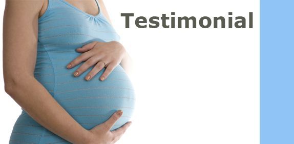 A pregnant woman in a blue tank top is holding her belly.