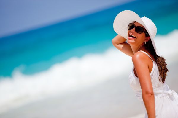 A woman wearing a white hat and sunglasses is standing on a beach.