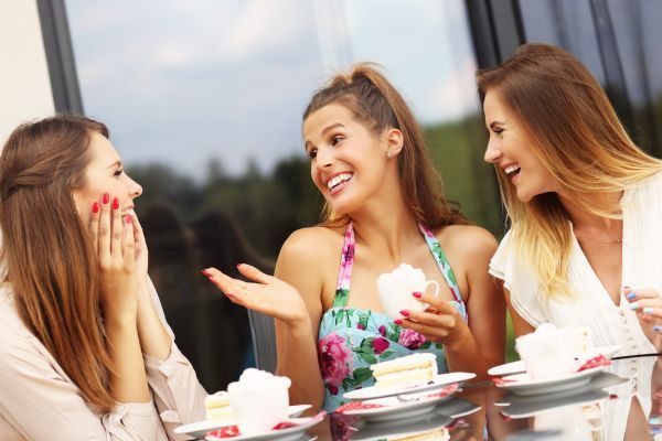 Three women are sitting at a table eating cake and talking.