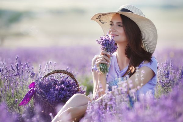 A woman is sitting in a field of lavender flowers holding a bouquet of flowers.