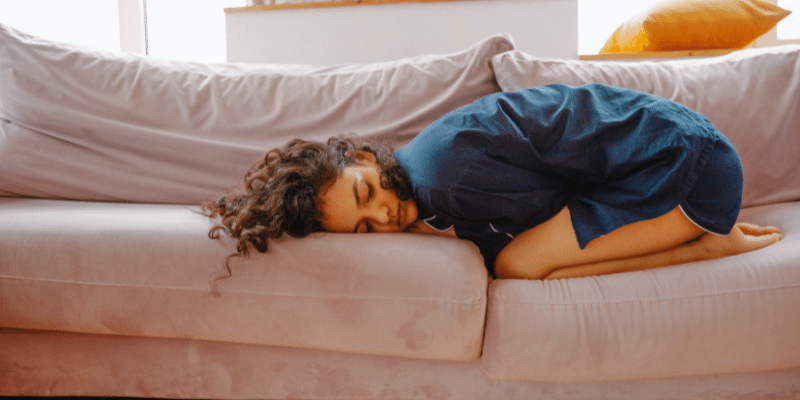 A woman is laying on a couch with her head on her knees.