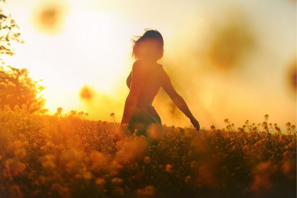 A woman is standing in a field of flowers at sunset.