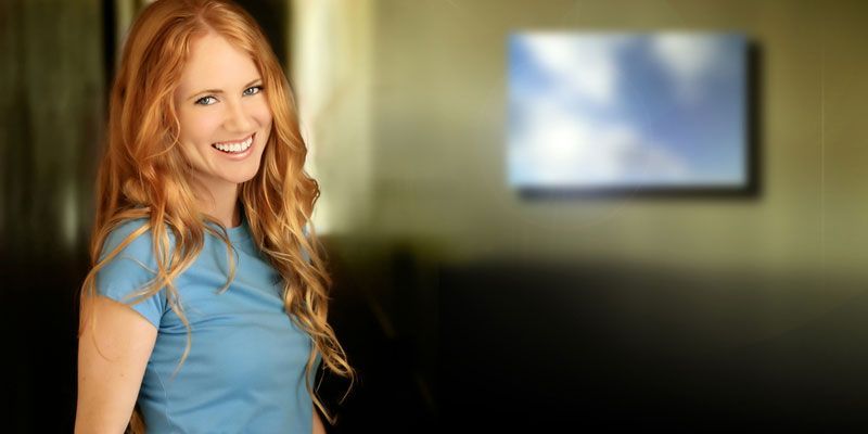 A woman with red hair is wearing a blue shirt and smiling.