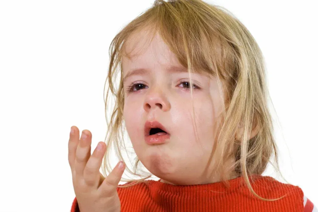A little girl is coughing while wearing a red sweater.