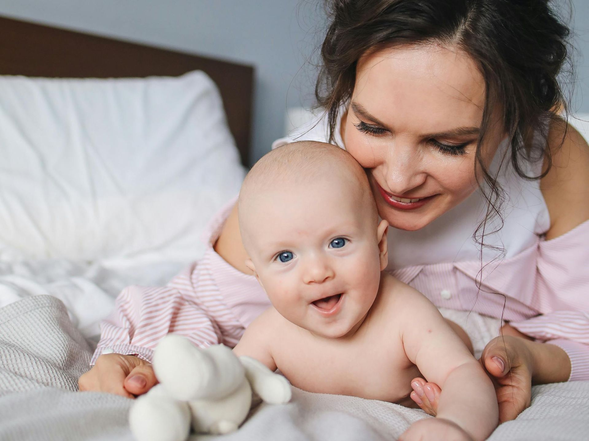 A woman is laying on a bed with a baby and a teddy bear.