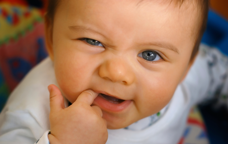 A baby is biting his finger in his mouth