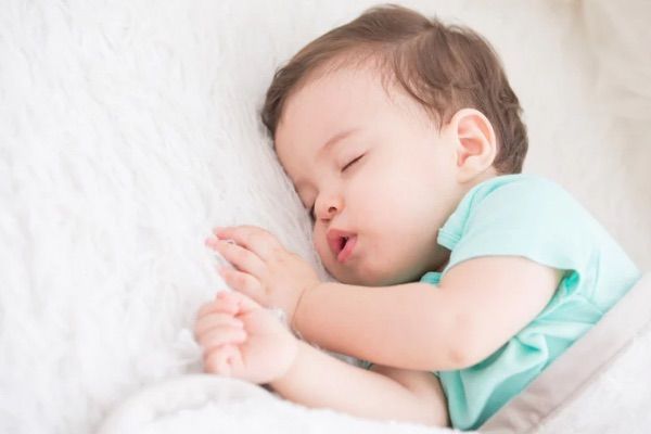 A baby is sleeping on a bed with a white blanket.