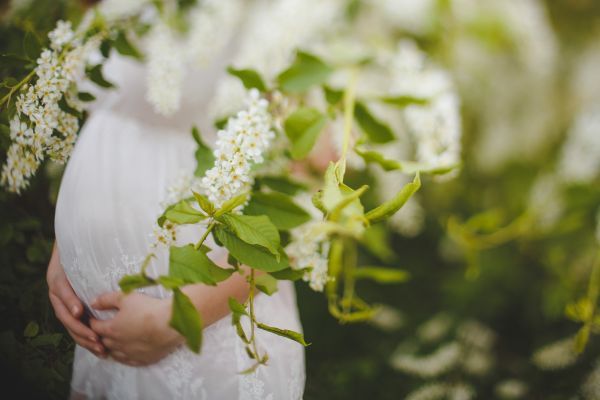A pregnant woman in a white dress is holding a bouquet of white flowers.