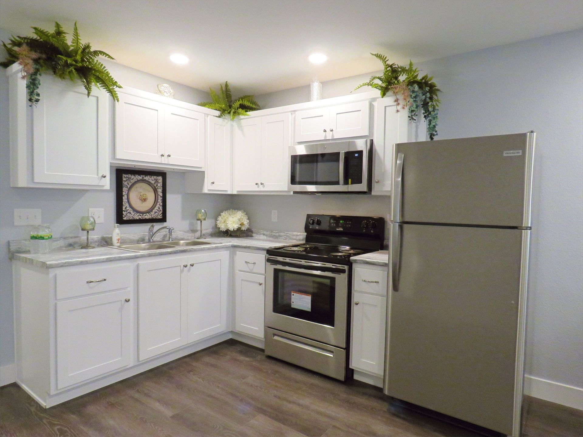 A kitchen with white cabinets , stainless steel appliances , a refrigerator , stove , microwave and sink.