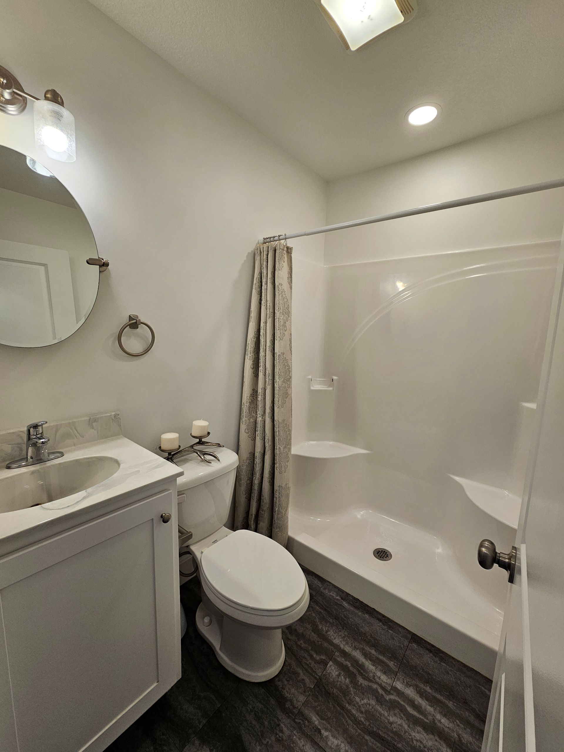 A bathroom with a toilet , sink , shower and mirror.