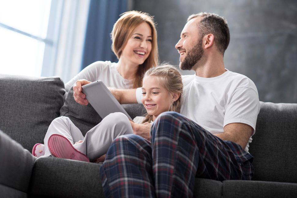 Una famiglia seduta insieme sul divano, sorridente mentre legge su un tablet in un soggiorno luminoso