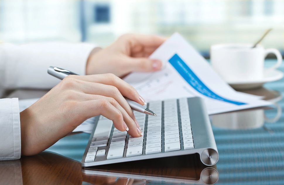 Mani che digitano su un laptop, con fogli e una tazza di caffè sulla scrivania