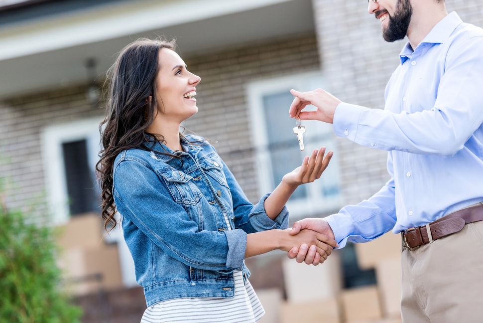 Due persone si stringono la mano fuori da una casa, mentre una consegna le chiavi all’altra
