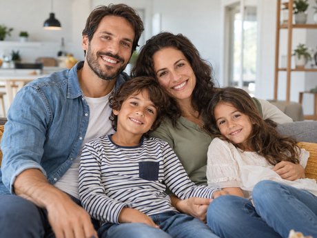 Famiglia sorridente di quattro persone seduta su un divano in un soggiorno luminoso