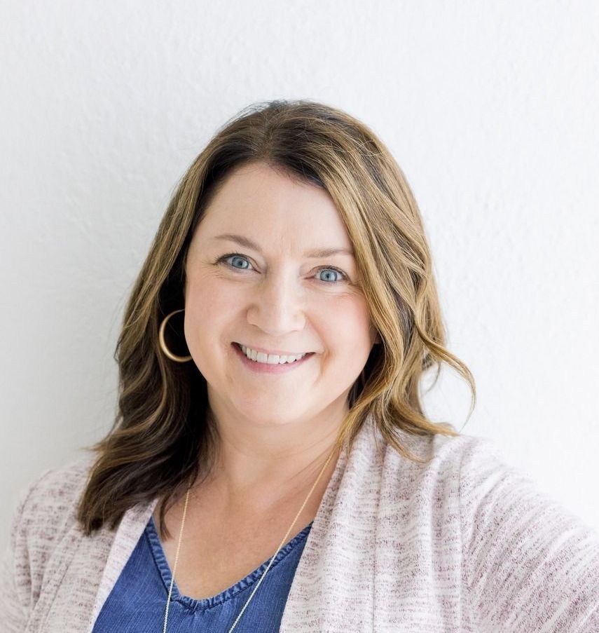 Woman smiling, wearing a pink cardigan and hoop earrings, against a white background.
