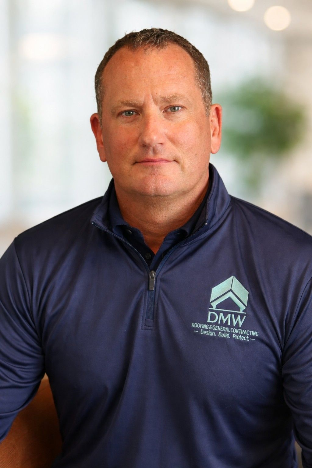 Man in black shirt with logo, smiling outdoors.