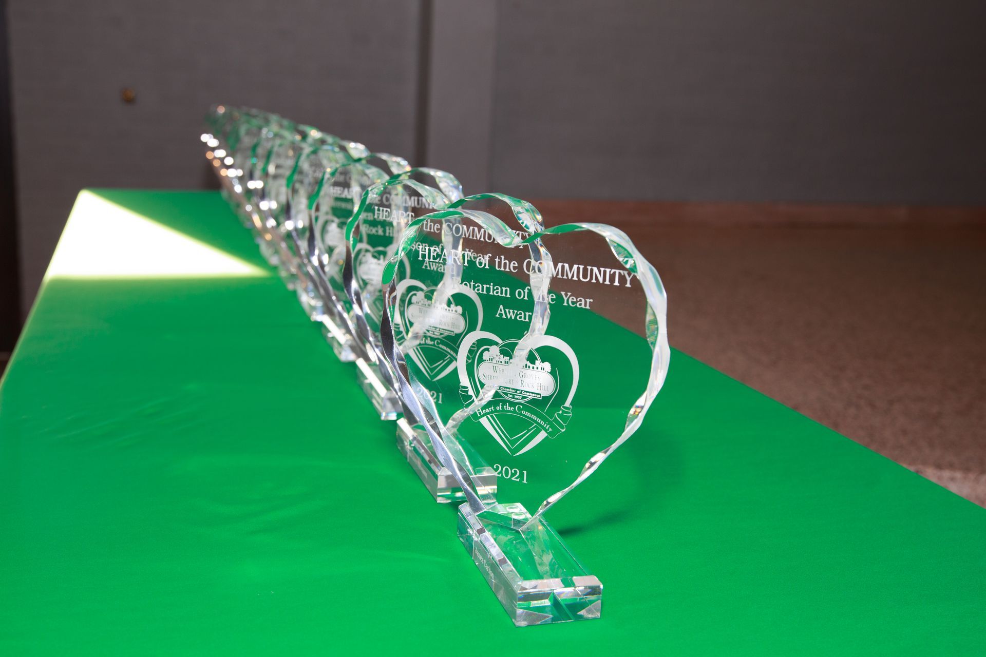 Crystal heart-shaped awards on a green surface, etched with text and a heart design, lined up.