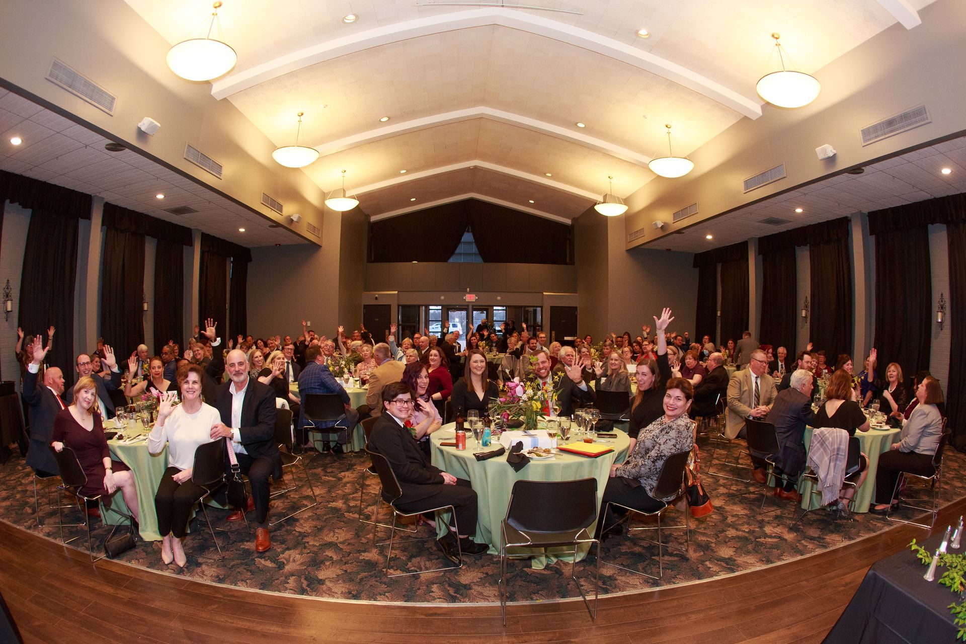 Large banquet hall with many people at tables, some waving, celebrating.