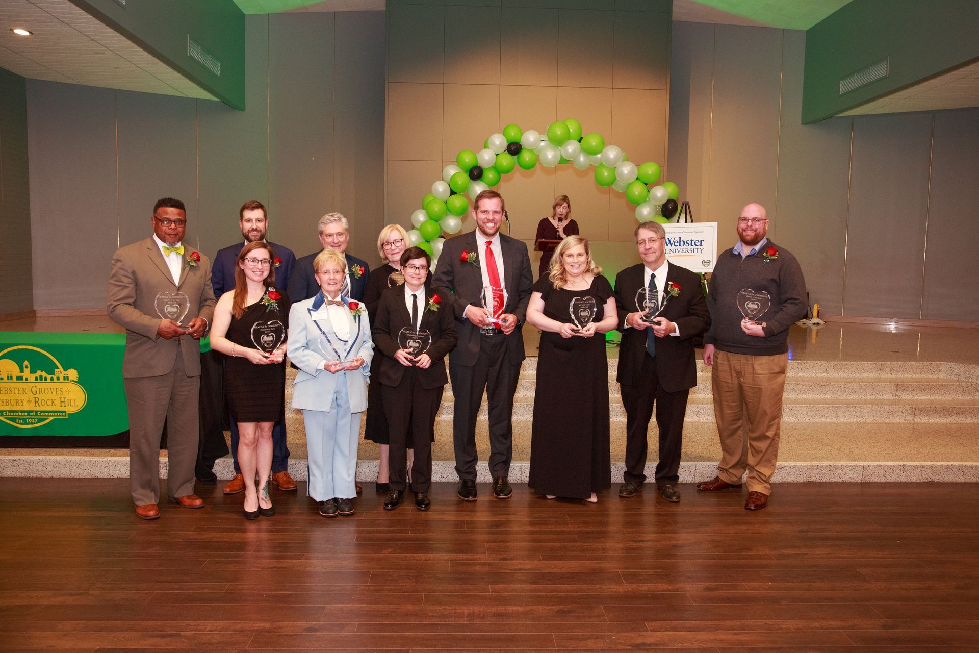 Group of people with awards, posing in front of a green and black balloon arch at an event.