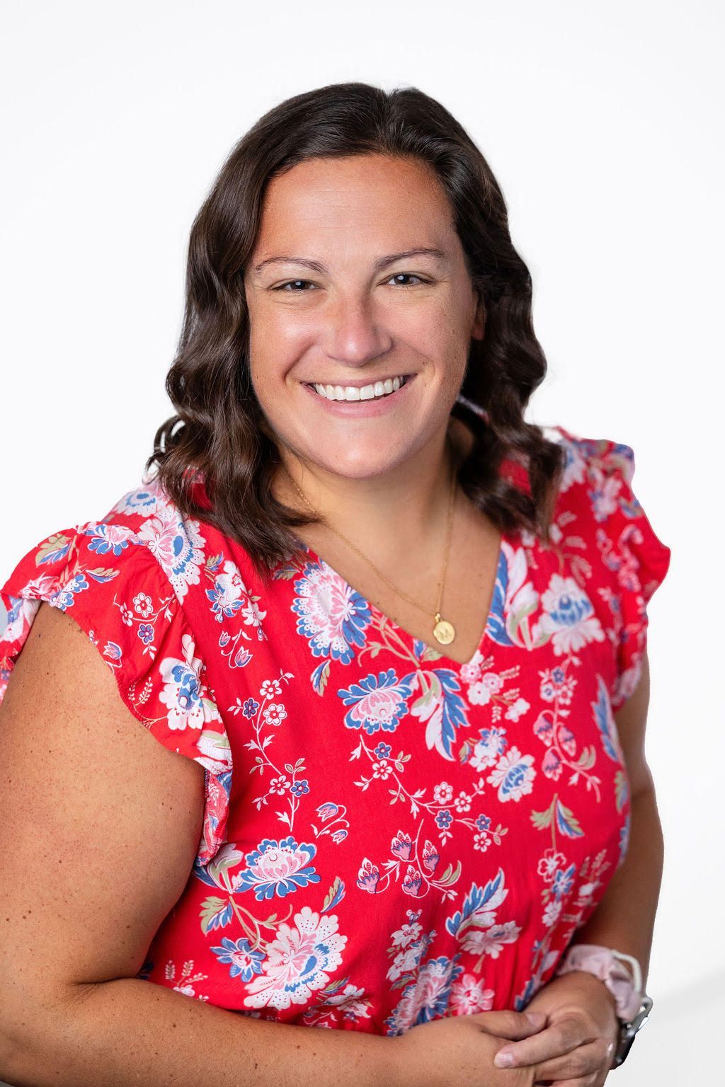 Woman smiling, wearing a red floral print top, looking at the camera.
