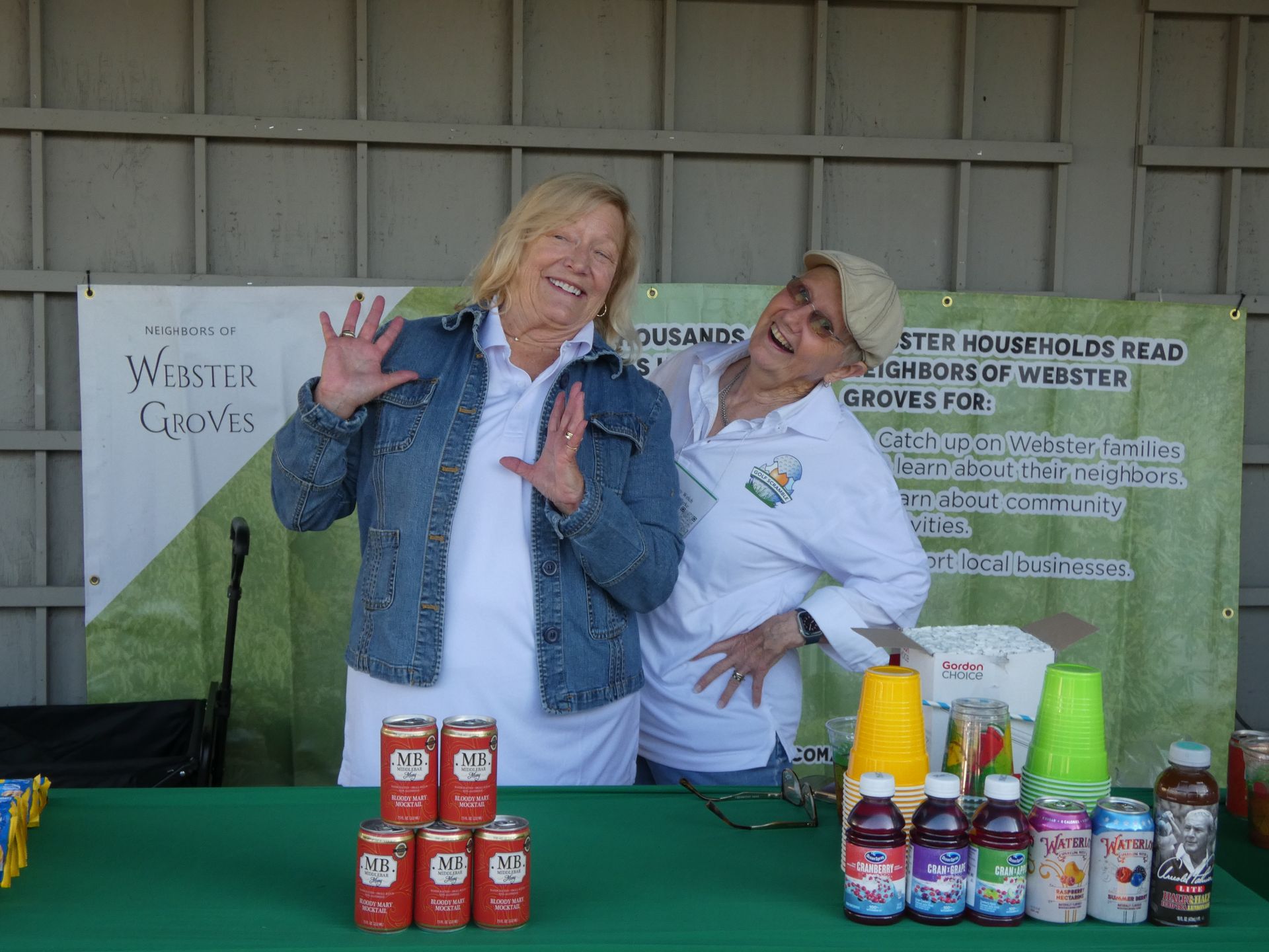 Two women at a booth with drinks, smiling, under a banner. Red cans stacked, colorful bottled drinks displayed.