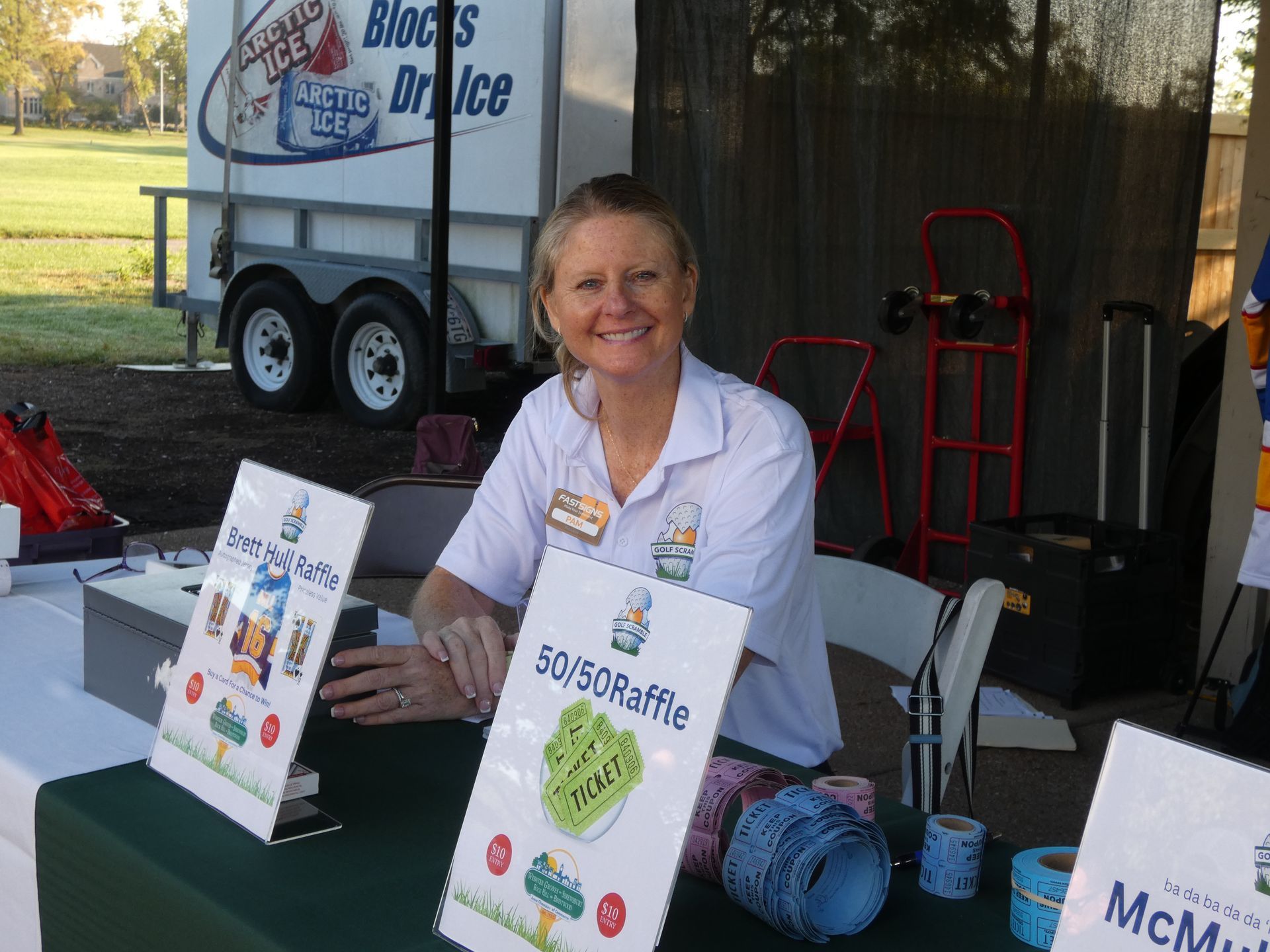 Woman behind a table selling raffle tickets, Blocks of Ice trailer in background.