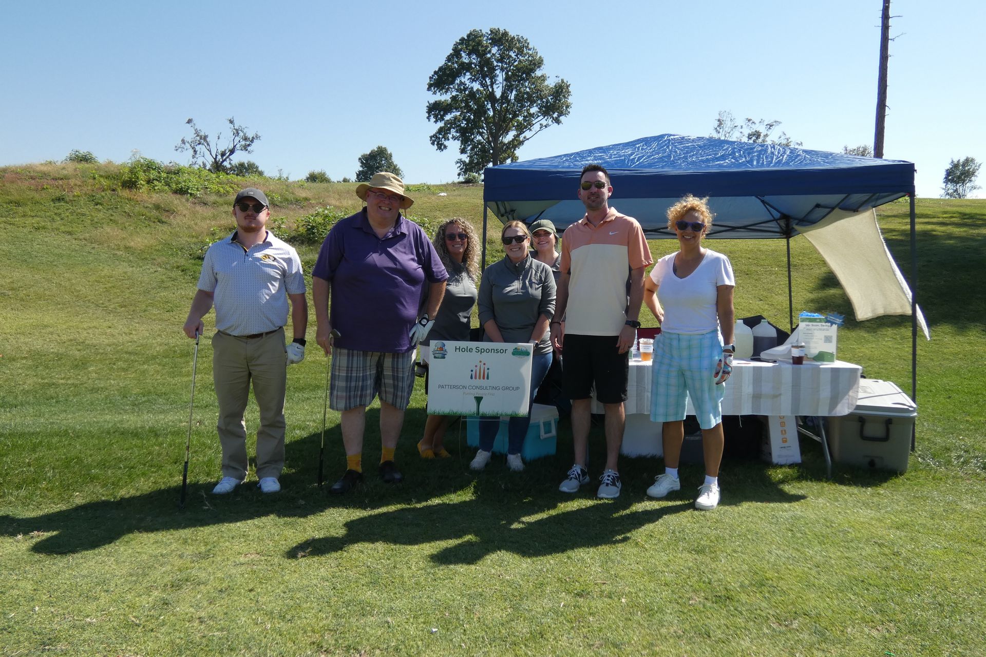 Group of people standing at a golf course refreshment stand on a sunny day.