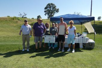 Group of people standing at a golf course refreshment stand on a sunny day.