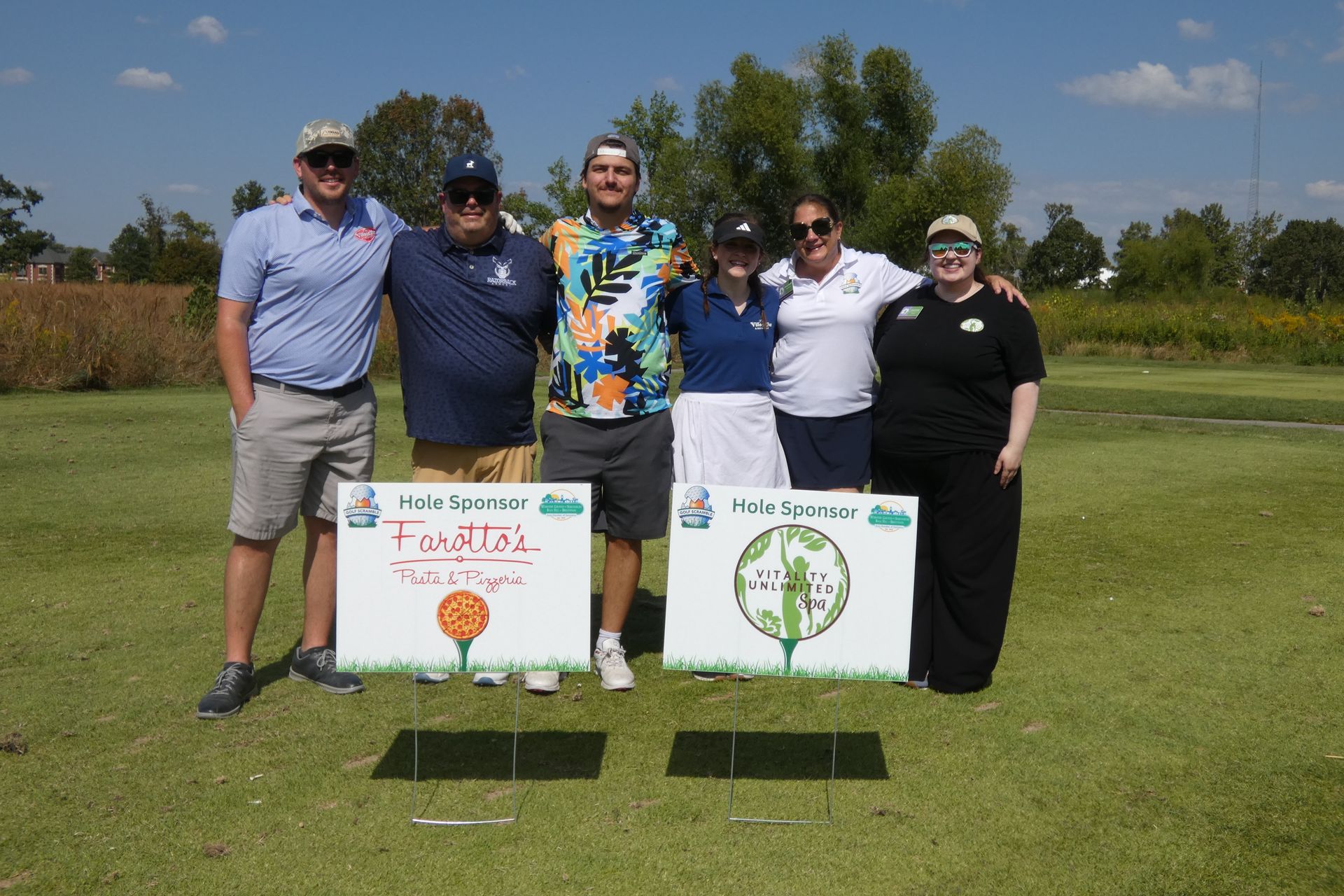 Group of people posing with signs at golf course on a sunny day.