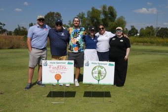 Group of people posing with signs at golf course on a sunny day.