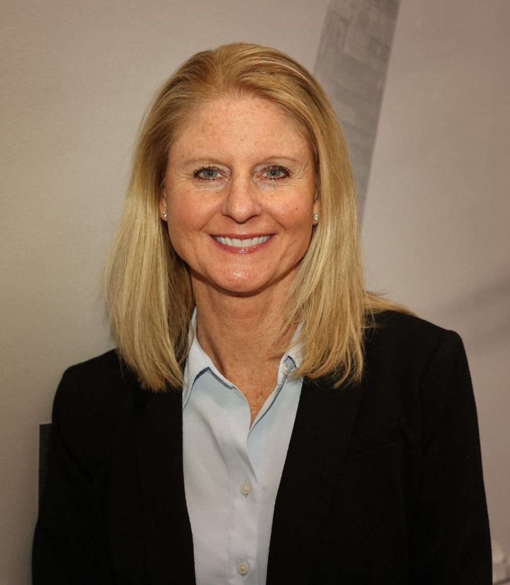 Woman with blonde hair wearing a black blazer and light blue shirt, smiling.